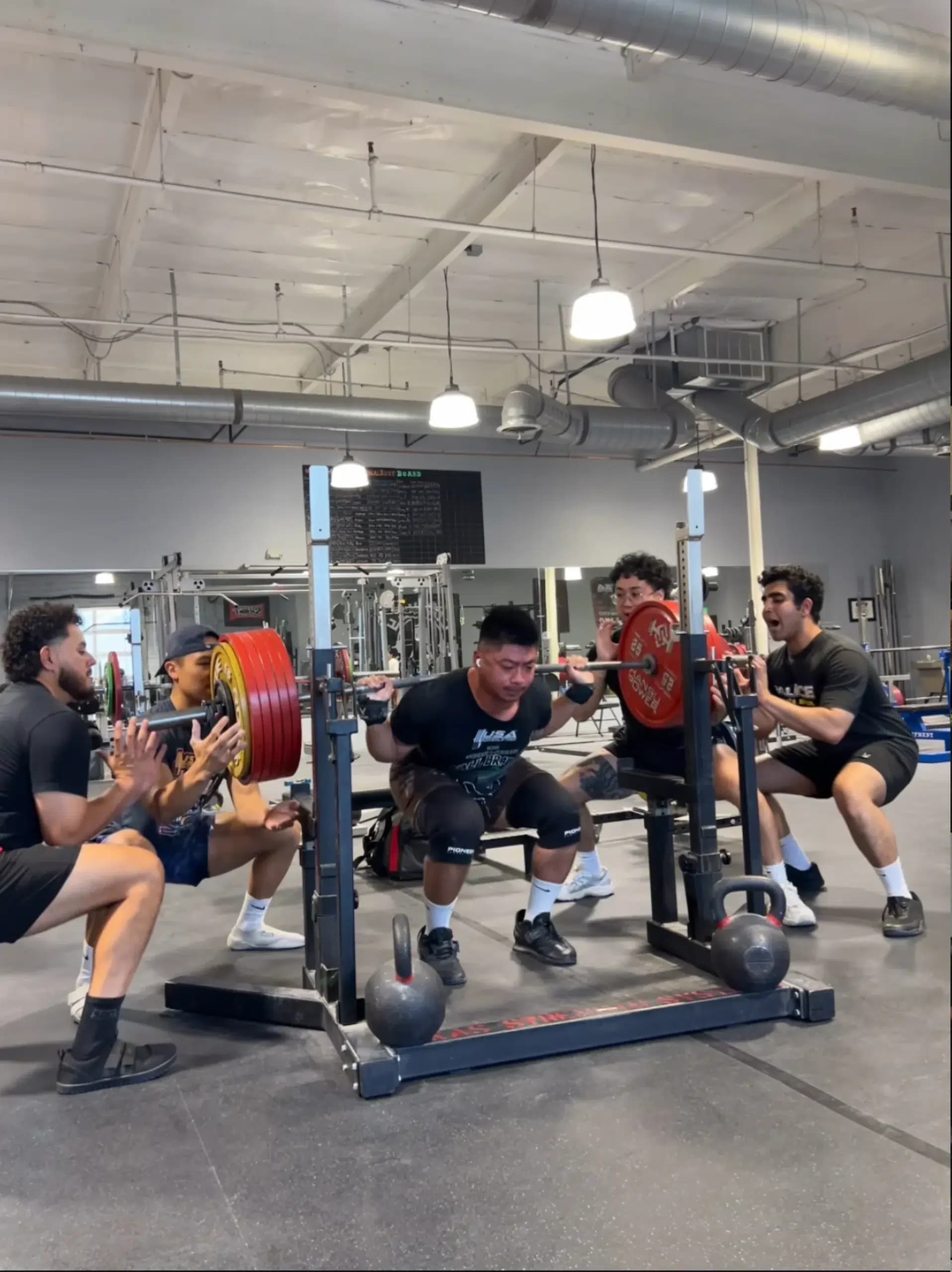 A group of Convoy Strength powerlifters squatting and spotting